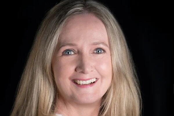 A white woman with blue eyes and blonde hair smiles at the camera