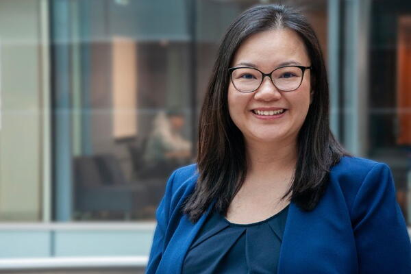 An asian woman wearing glasses and a blue blazer smiles at the camera