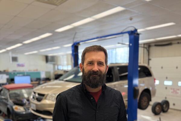 A man with a beard standing in front of a car shop 