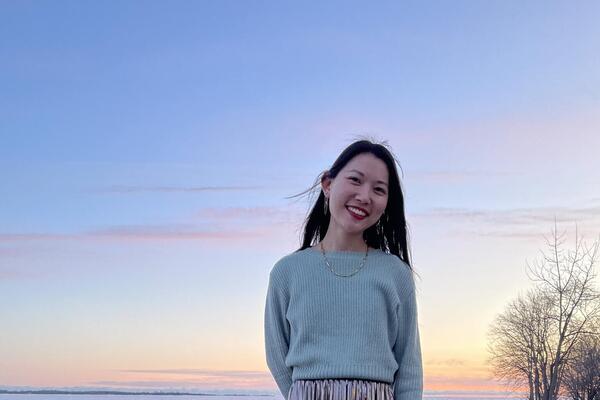 An Asian woman posing on a water front in a blue sweater and metallic long skirt in the winter at sunset