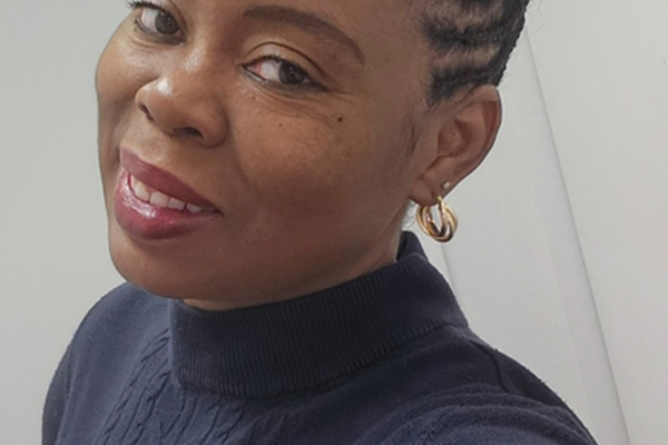 A black woman smiles at a camera with a black turtleneck on and a white background