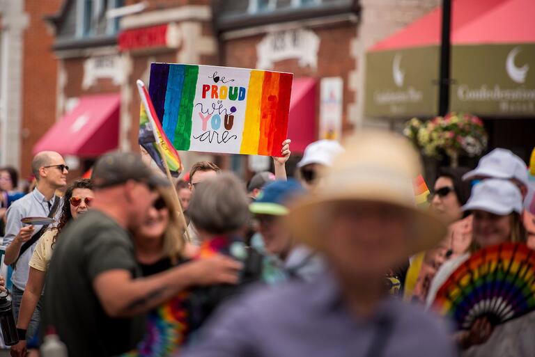 People Marching in a Pride Parade with a sign that reads, "Be PRoud of You"