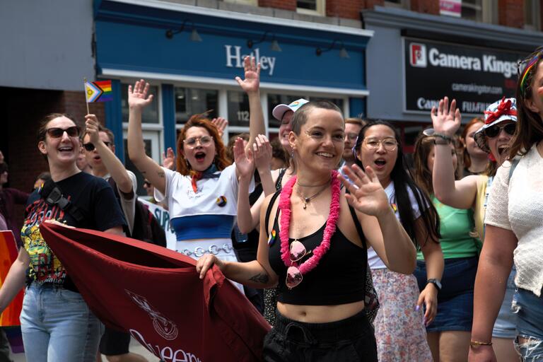Students marching in Pride Parade with Faculty of Education Banner while waving 