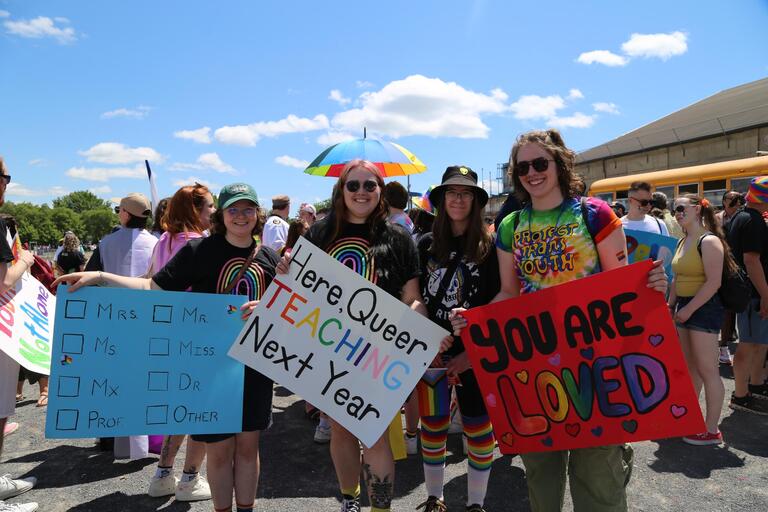 People wearing rainbow cloths with signs that say you are loved and here queer teaching next year