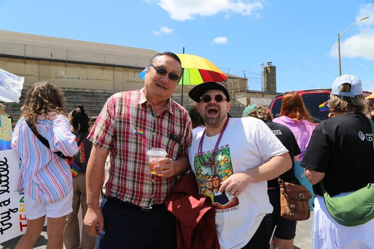Two men look at the camera with rainbow outfits on
