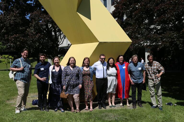People in summer clothing smiling in front of a yellow sculpture.