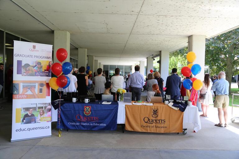 Two tables with Queen's logos sit between two tricolour sets of balloons.