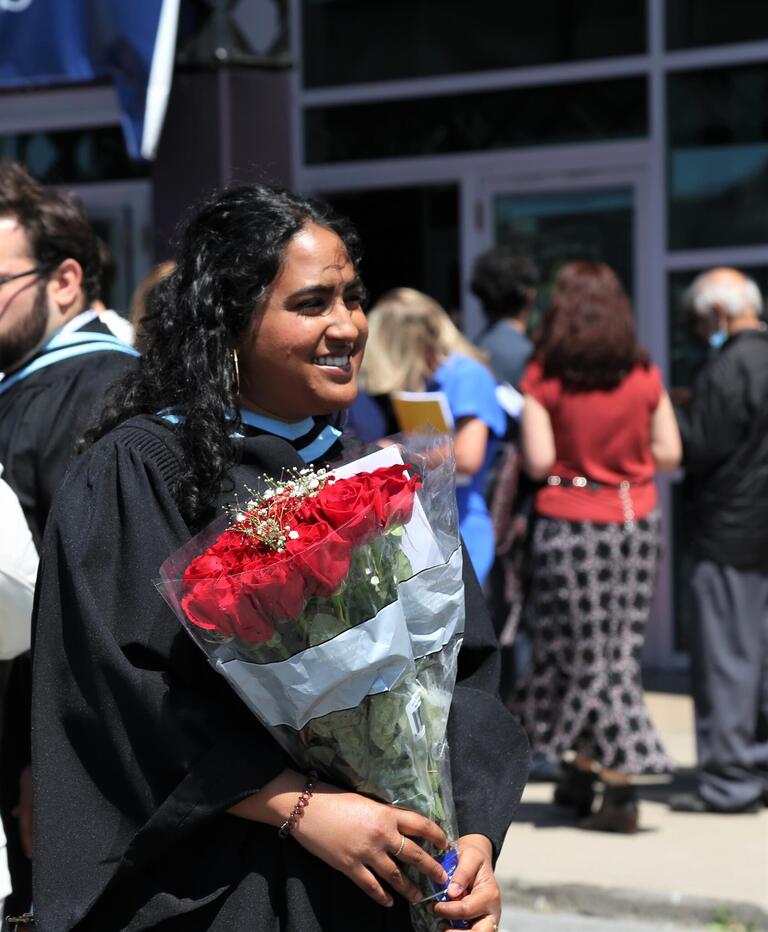 A graduate poses for a photo holding red roses.