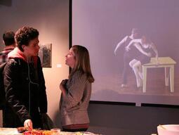 Two people speaking in front of a film of dancing.