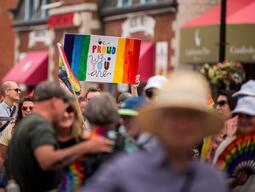 People Marching in a Pride Parade with a sign that reads, "Be PRoud of You"