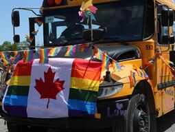 A yellow school bus covered in pride flags 