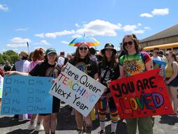 People wearing rainbow cloths with signs that say you are loved and here queer teaching next year