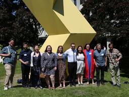 People in summer clothing smiling in front of a yellow sculpture.