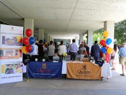 Two tables with Queen's logos sit between two tricolour sets of balloons.