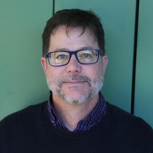 A white man with glasses and a beard looks at the camera. 