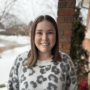 A woman with light brown hair smiles in front of a snowy background with a cozy leopard print sweater on. 
