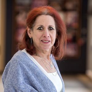 Andrea Martin smiling in a hallway with a grey cardigan and white shirt on