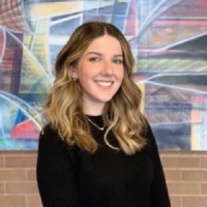 Andrea Hill smiling in front of a colourful piece of art with a black top on