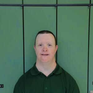 Brian is grinning at the camera. He is wearing a green golf shirt and has short brown hair.