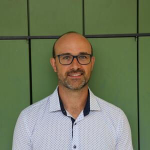 Casey grins at the camera. He is wearing glasses and a white polo shirt. 