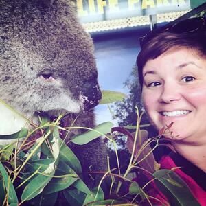 Nathalie smiles at the camera. she has short dark brown hair. She is standing very close to a koala