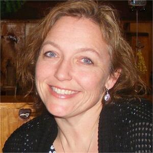 Tracy smiles at the camera, her hair is chin length and dark blonde. She is wearing a black cardigan. 