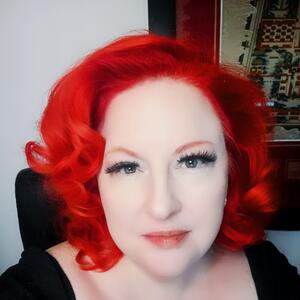 Holly looks at the camera. She has bright red, shoulder length curly hair.
