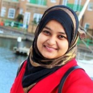 Sumaiya smiles at the camera wearing a red coat.