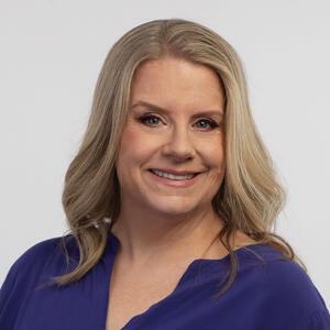 A white woman with blond hair wearing a blue blouse with a white background