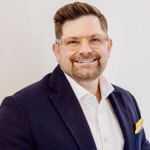 A man wearing a suit smiling at the camera wearing glasses 