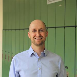 Kyle Cummings-Bentley smiles in a hallway in front of a wall of green lockers.