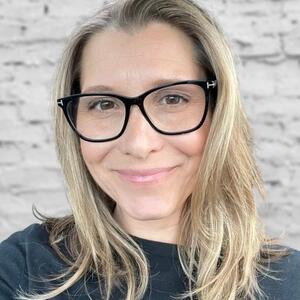 Laura Pugliese-Muir smiles in front of a brick wall.