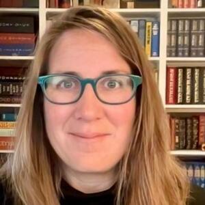 Lydia Scholle-Cotton smiles in front of a bookshelf wearing glasses.