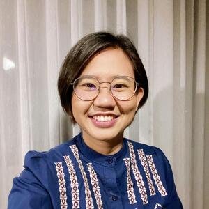 Poonyawee Jirarattanawan smiles inside wearing glasses and a patterned blue button-down shirt.