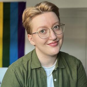 Photo of Ren Challacombe wearing glasses and a green button down shirt inside.