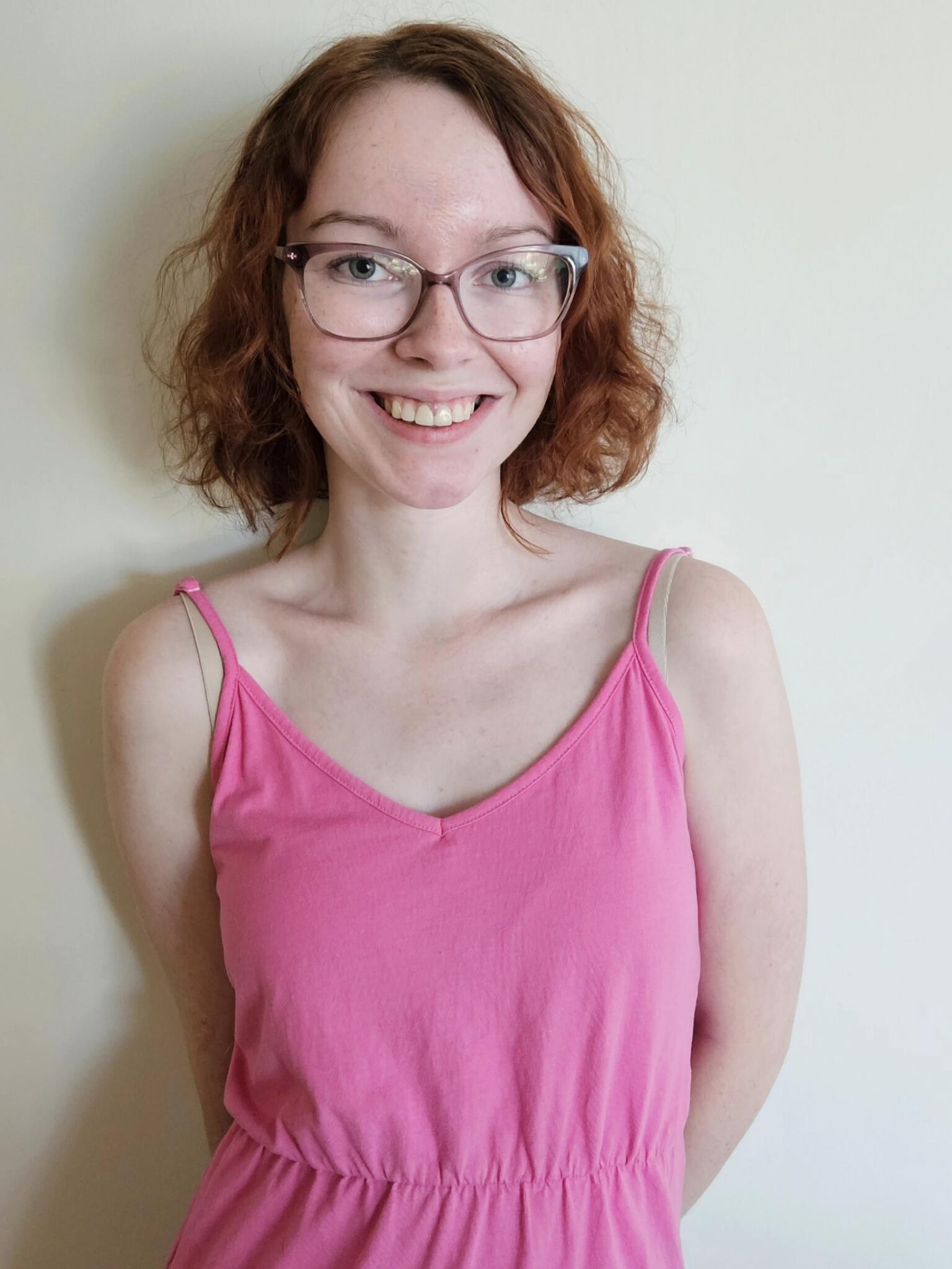 Claire smiles at the camera wearing a bright pink dress against a white background