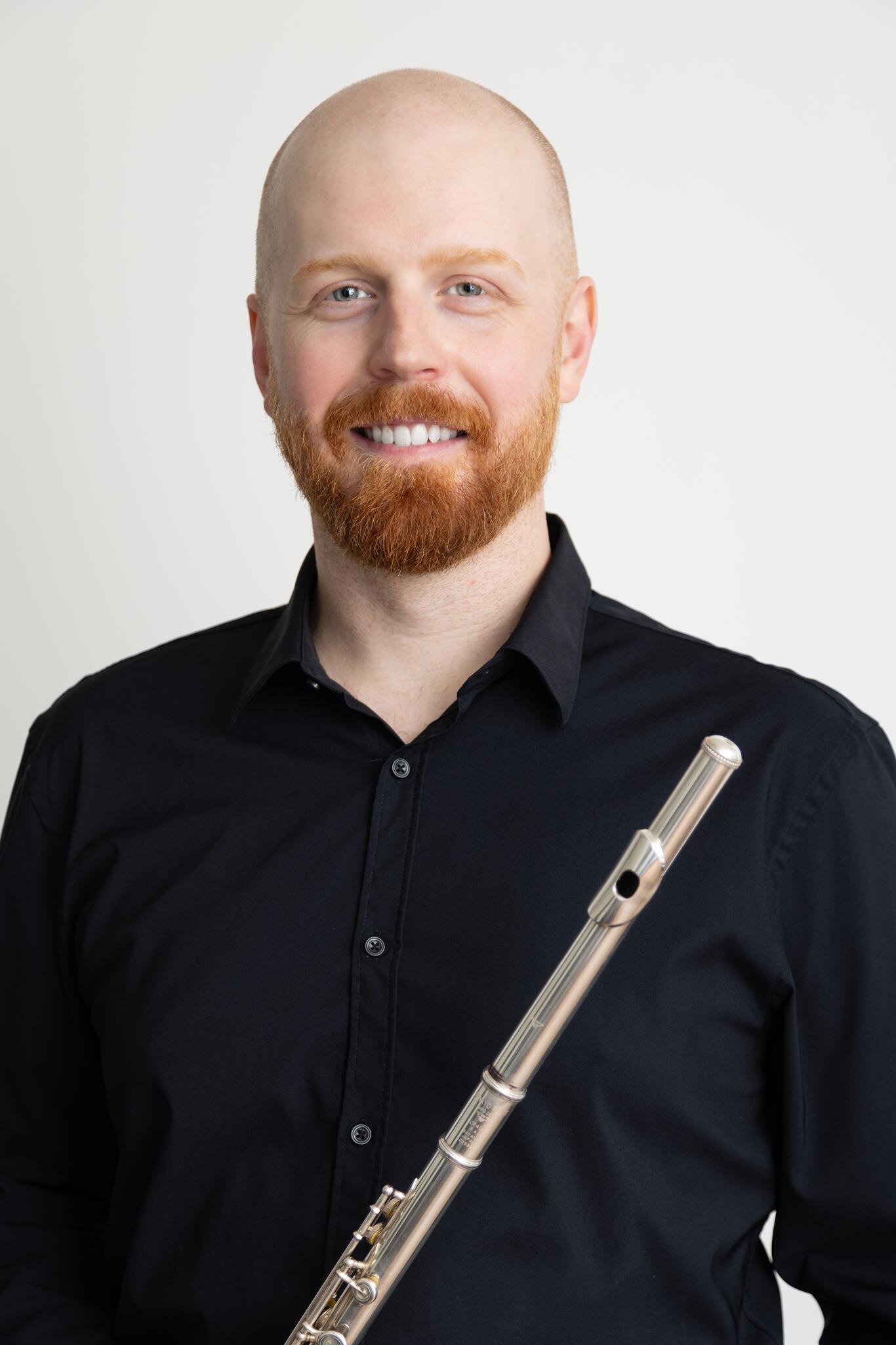 Graham smiles against a white background holding a flute.