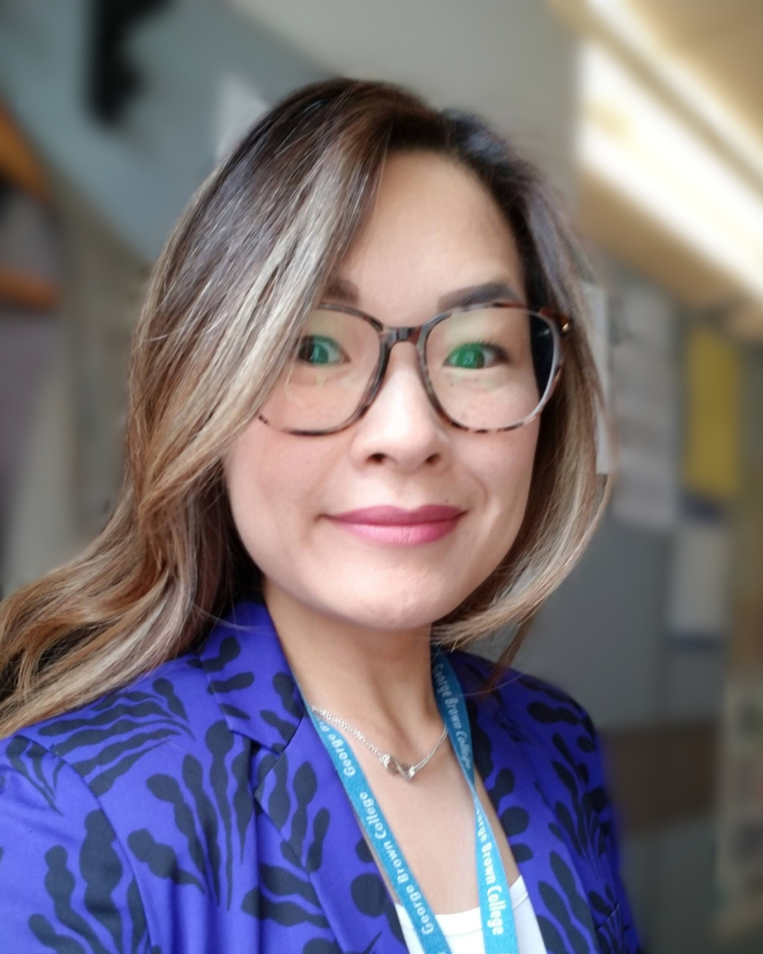 Sandra smiles at the camera wearing a purple blazer and glasses