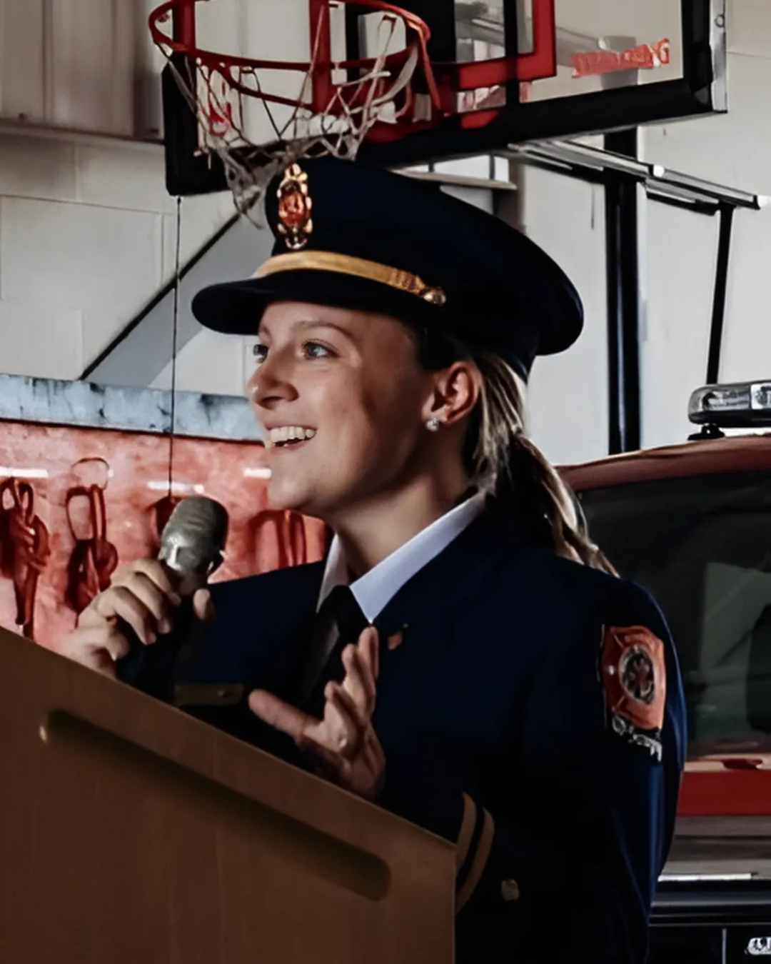 Kristy-Lynn smiles while holding a microphone and gesticulating. She is wearing a uniform. 