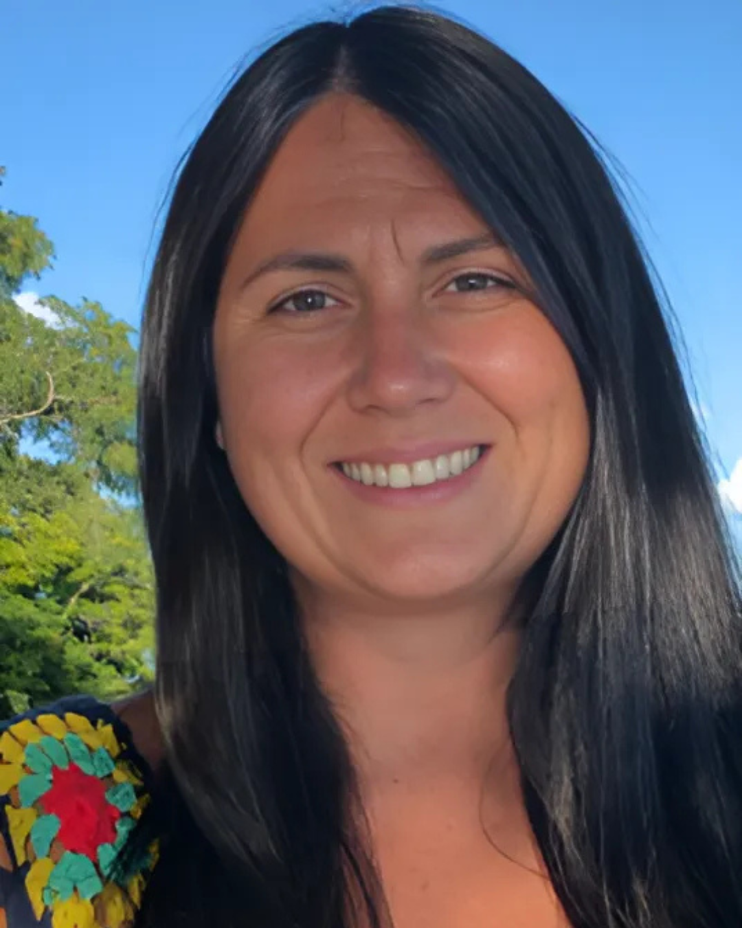 Jennifer, with long black hair, smiles at the camera against a bright blue sky
