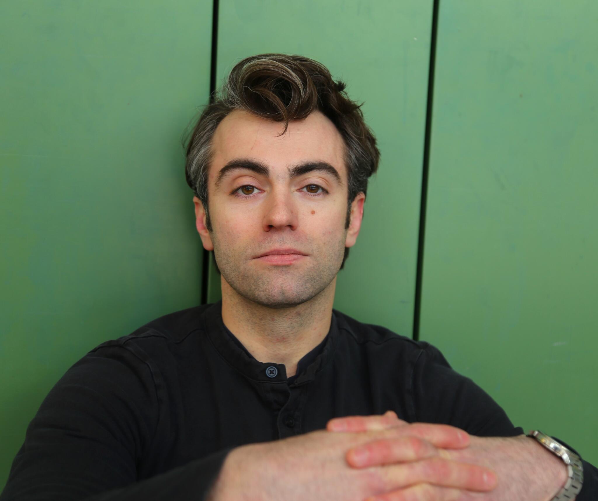 Nathan looks calmly into the camera against a green background