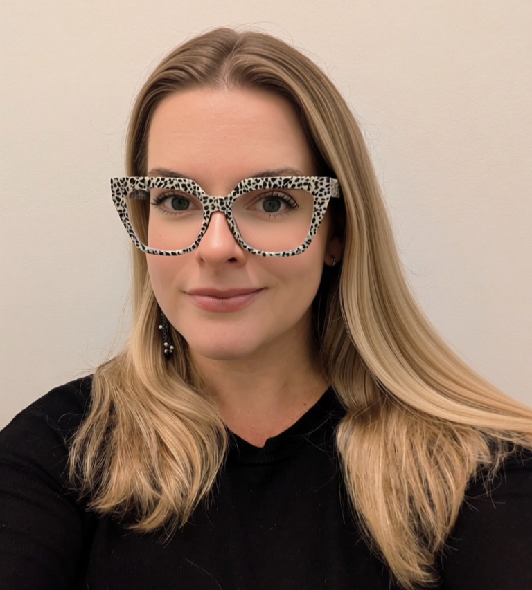 A blonde woman wearing glasses smiles at the camera