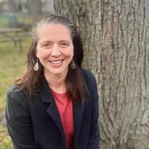 A woman smiles in front of a tree