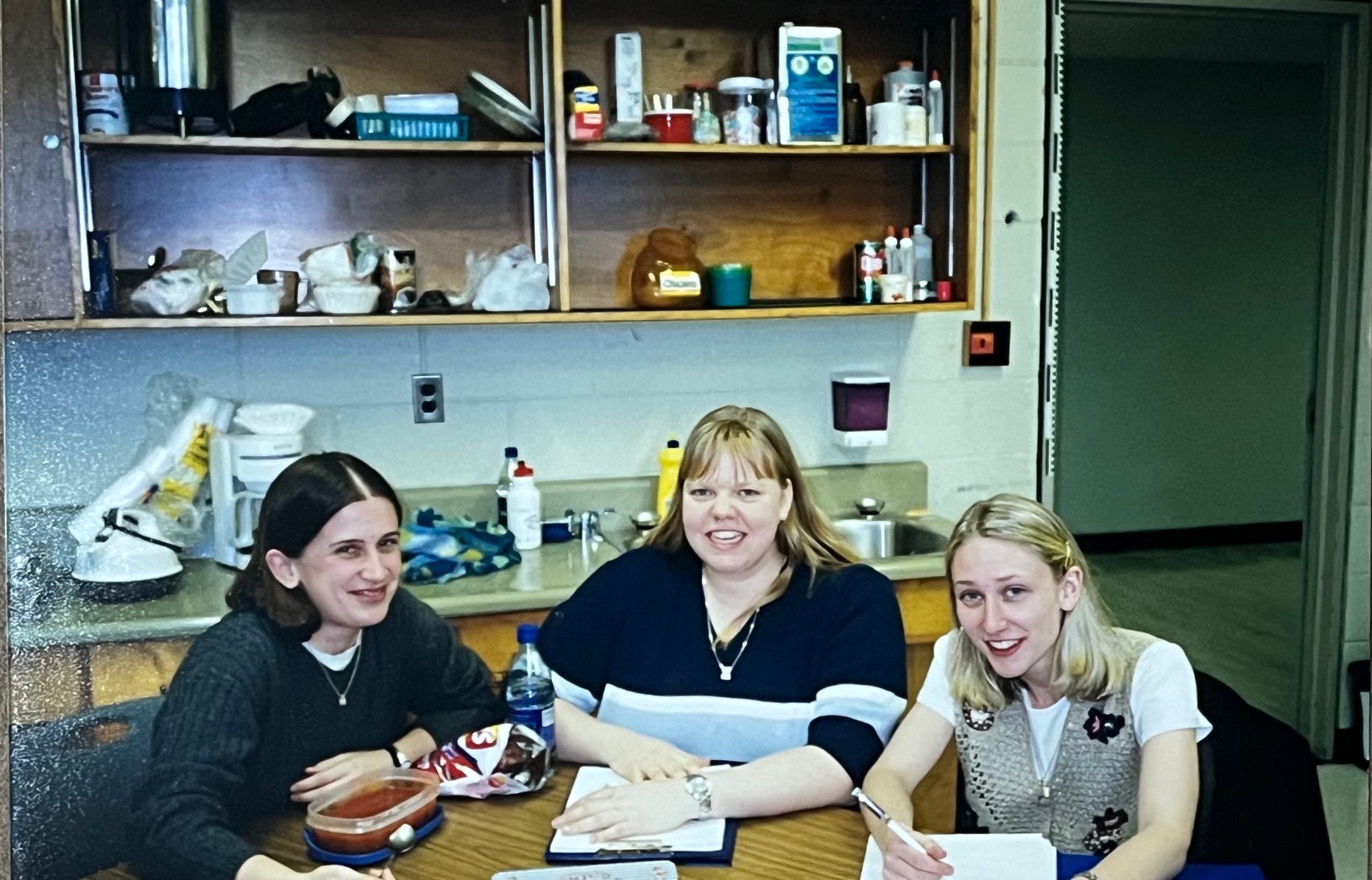 Three students sit around a table smiling.