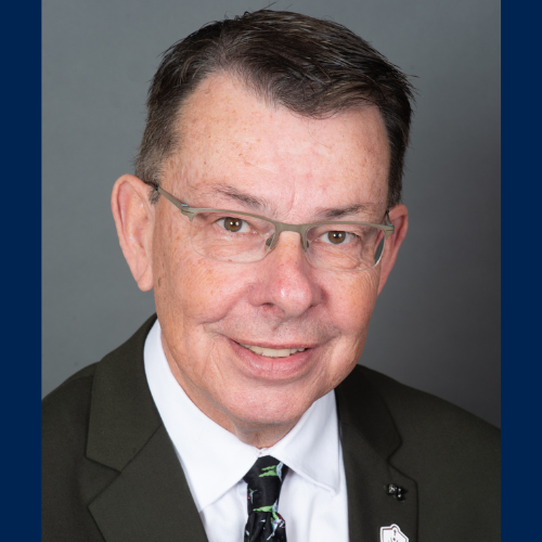 Brian Evoy smiles wearing glasses and a suit and tie.