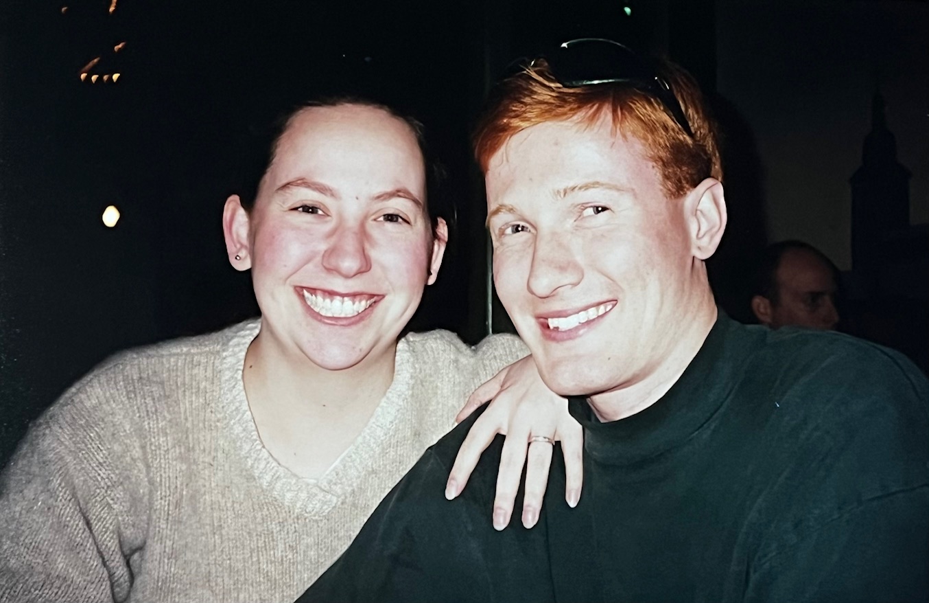 Two students smile in a film photo. The background is obscured.