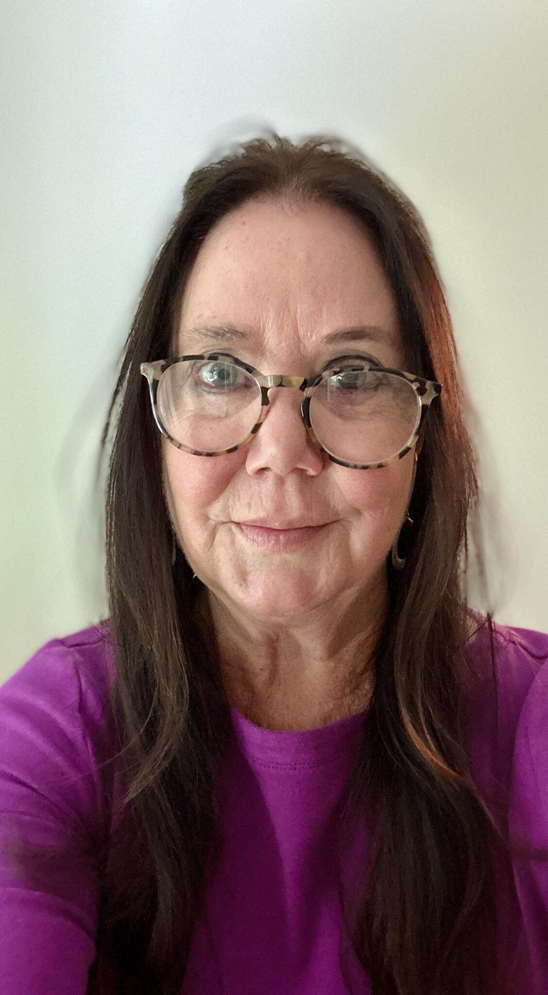 Erin Kelly smiles wearing a purple shirt and glasses.