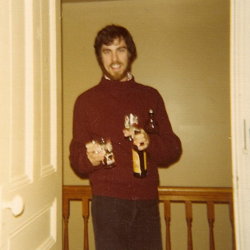 Gary Bauer in a photo from 1977 wearing a brown sweater and holding bottles and glasses