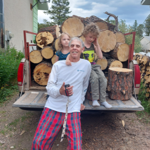 Gary Bauer smiles while sitting on the back of truck hauling lumber. Two children sit behind him on the same truck.