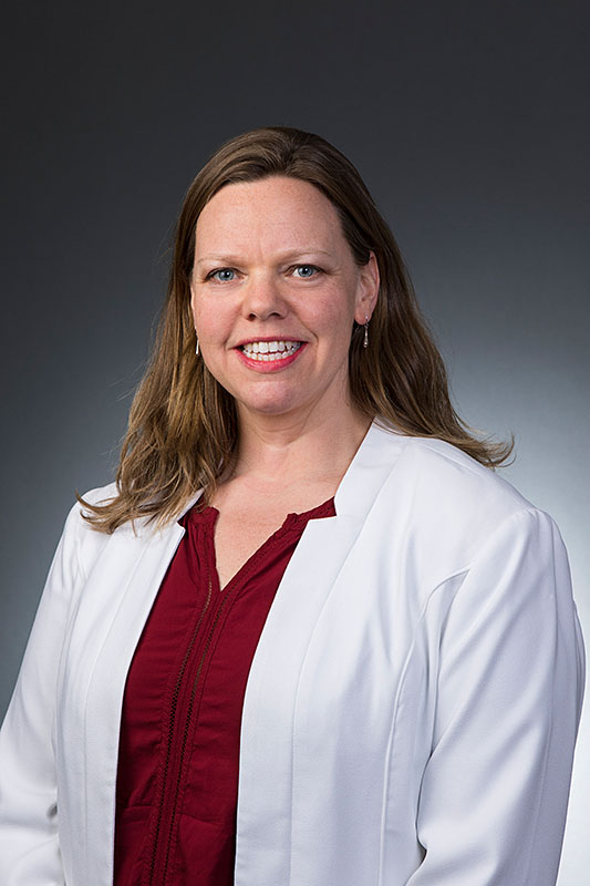 Julia Allen smiles in front of a grey background wearing a white coat.